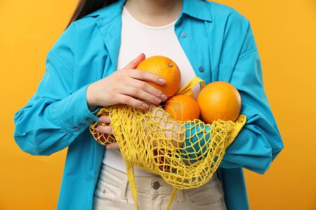 Téléchargez les photos : Femme avec sac à ficelle d'oranges fraîches sur fond orange, gros plan - en image libre de droit