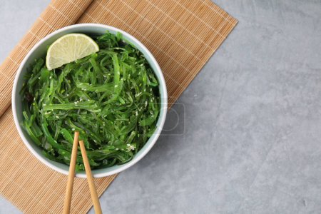 Tasty seaweed salad in bowl served on gray table, top view. Space for text