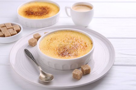 Téléchargez les photos : Délicieuse crème brulée dans des bols, gousses de vanille, cubes de sucre et café sur table en bois blanc - en image libre de droit