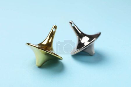 Golden and silver spinning tops on light blue background, closeup