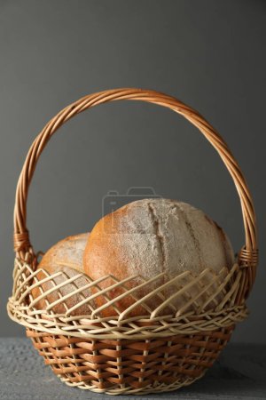 Wicker basket with fresh bread on grey wooden table