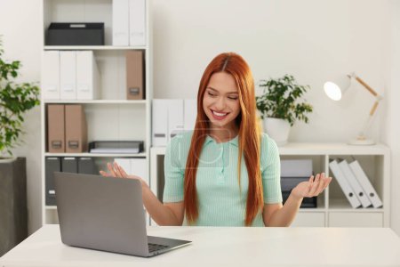 Foto de Mujer joven que tiene chat de vídeo a través de ordenador portátil en la mesa en la oficina - Imagen libre de derechos