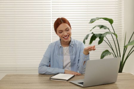 Foto de Mujer joven que tiene video chat a través de ordenador portátil en la mesa de madera en el interior - Imagen libre de derechos
