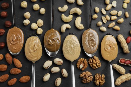 Photo for Tasty nut butters in spoons and raw nuts on dark gray table, flat lay - Royalty Free Image