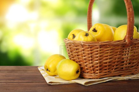 Fresh ripe quinces in wicker basket on wooden table outdoors. Space for text
