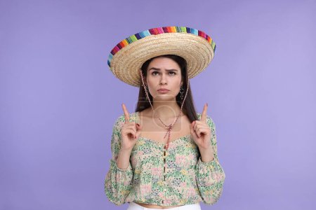 Mujer joven en sombrero mexicano señalando algo sobre fondo violeta