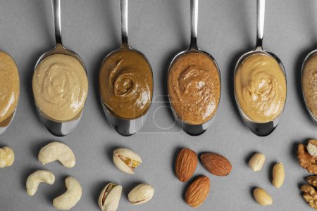 Photo for Tasty nut butters in spoons and raw nuts on gray table, flat lay - Royalty Free Image