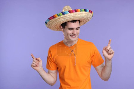Joven con sombrero mexicano señalando algo sobre fondo violeta