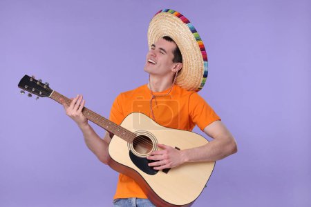 Joven en sombrero mexicano tocando la guitarra sobre fondo violeta