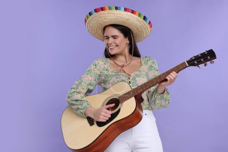 Mujer joven en sombrero mexicano tocando la guitarra sobre fondo violeta