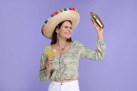 Mujer joven en sombrero mexicano sombrero con cóctel y coctelera sobre fondo violeta