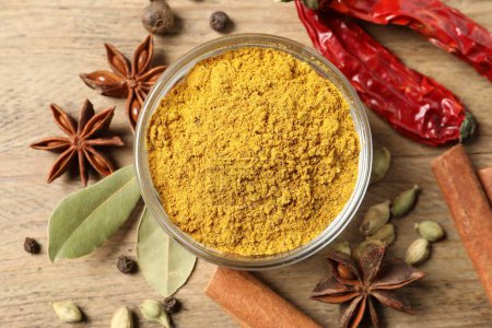 Curry powder in bowl and other spices on wooden table, flat lay