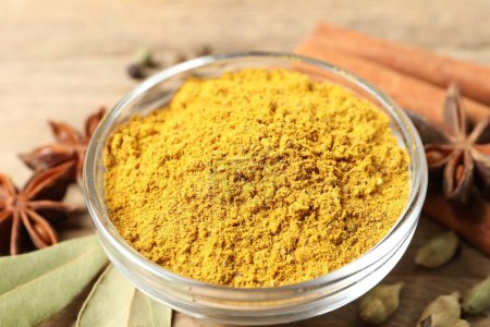 Curry powder in bowl and other spices on wooden table, closeup