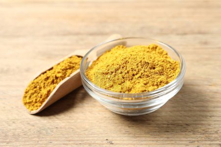 Curry-Pulver in Schüssel und Schaufel auf Holztisch, Nahaufnahme