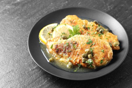 Delicious chicken piccata with herbs and lemons on black table