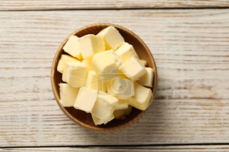 Tasty butter cubes in bowl on light wooden table, top view