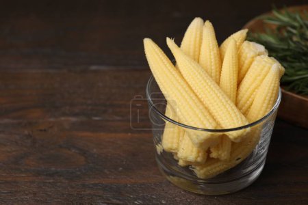 Tasty fresh yellow baby corns in glass on wooden table, space for text