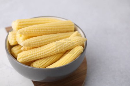Tasty fresh yellow baby corn in bowl on white table, space for text