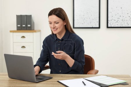 Foto de Mujer teniendo chat de vídeo a través de ordenador portátil en la mesa de madera en la oficina - Imagen libre de derechos