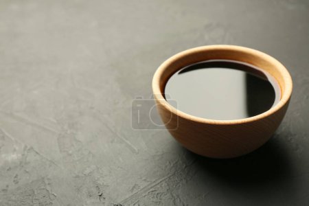 Soy sauce in wooden bowl on black textured table. Space for text