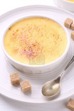 Téléchargez les photos : Délicieuse crème brulée dans un bol, cubes de sucre et cuillère sur table blanche - en image libre de droit