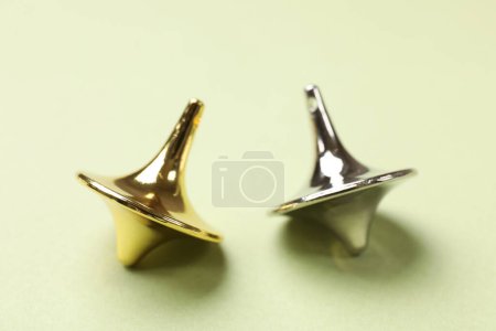 Golden and silver spinning tops on green background, closeup