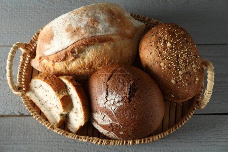Cesta de mimbre con diferentes tipos de pan fresco en la mesa de madera gris, vista superior