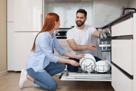 Photo for Happy couple loading dishwasher with plates in kitchen - Royalty Free Image
