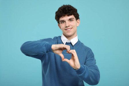 Téléchargez les photos : Jeune homme heureux montrant geste de coeur avec les mains sur fond bleu clair - en image libre de droit