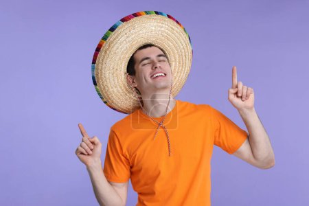 Joven con sombrero mexicano señalando algo sobre fondo violeta