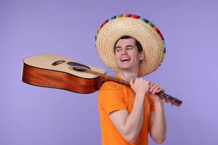 Hombre joven en sombrero mexicano con guitarra sobre fondo violeta