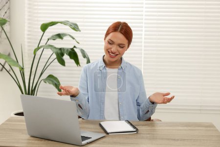 Foto de Mujer joven que tiene video chat a través de ordenador portátil en la mesa de madera en el interior - Imagen libre de derechos
