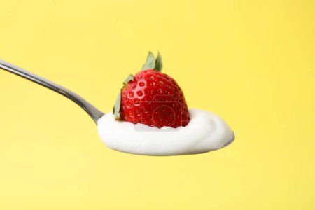 Cuchara con yogur y fresa sobre fondo amarillo, primer plano