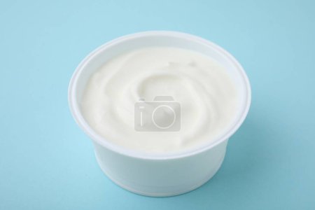 Delicioso yogur natural en taza de plástico sobre fondo azul claro
