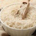 Raw basmati rice in bowl and scoop on cloth, closeup