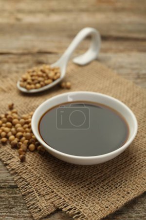 Soy sauce in bowl and beans on wooden table, closeup