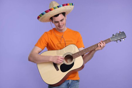 Joven en sombrero mexicano tocando la guitarra sobre fondo violeta