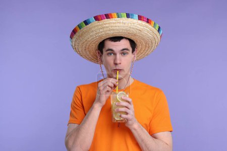 Joven en sombrero mexicano bebiendo cóctel sobre fondo violeta