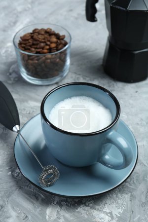 Mini batidora (espuma de leche), leche batida en taza y granos de café en mesa texturizada gris