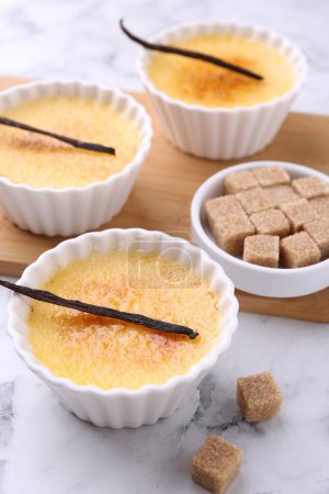 Téléchargez les photos : Délicieuse crème brulée dans des bols, gousses de vanille et cubes de sucre sur table en marbre blanc - en image libre de droit