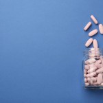 Bottle of pink vitamin capsules on blue background, top view. Space for text