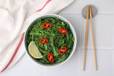 Tasty seaweed salad in bowl served on white tiled table, top view