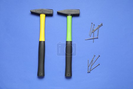 Hammers and metal nails on blue background, top view