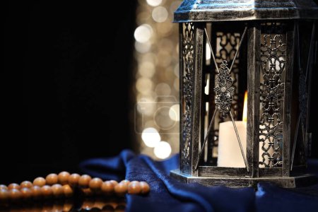 Arabic lantern and misbaha on table against blurred lights, closeup. Space for text