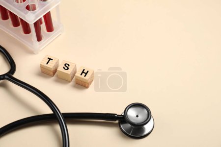 Endocrinology. Stethoscope, wooden cubes with thyroid hormones and blood samples in test tubes on beige background. Space for text