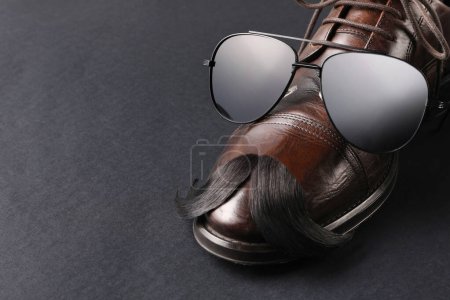 Téléchargez les photos : Moustache artificielle, chaussures et lunettes de soleil sur fond noir, gros plan. Espace pour le texte - en image libre de droit