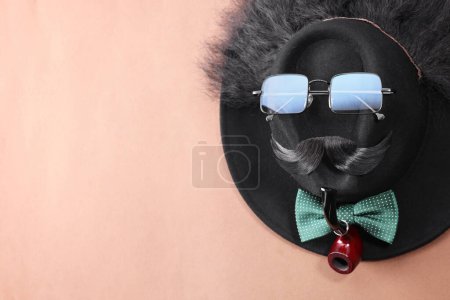 Téléchargez les photos : Visage d'homme fait de moustache artificielle, lunettes de soleil et chapeau sur fond brun, vue de dessus. Espace pour le texte - en image libre de droit