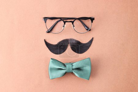 Téléchargez les photos : Visage d'homme fait de moustache artificielle, lunettes et noeud papillon sur fond brun, vue de dessus - en image libre de droit