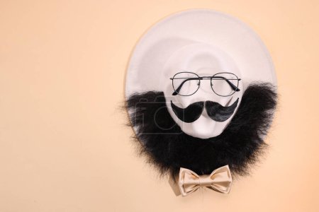 Téléchargez les photos : Visage d'homme fait de moustache artificielle, barbe et lunettes sur fond beige, vue de dessus. Espace pour le texte - en image libre de droit