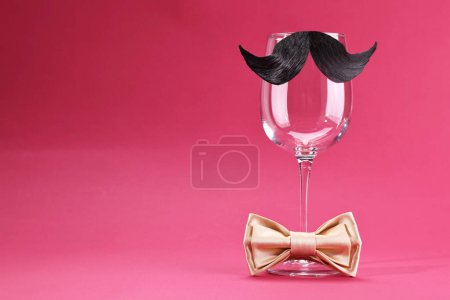 Téléchargez les photos : Visage d'homme fait de moustache artificielle, noeud papillon et verre de vin sur fond cramoisi. Espace pour le texte - en image libre de droit
